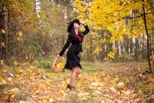 young attractive witch walks in the autumn orange forest. helloween concept