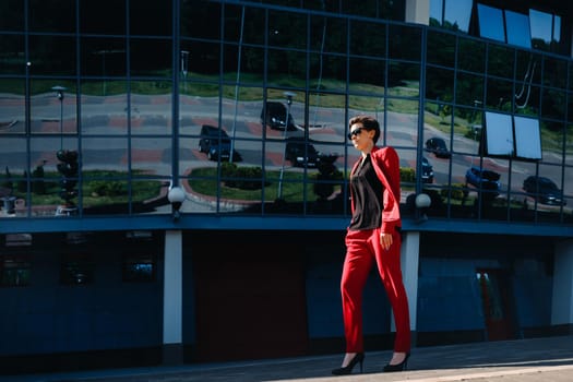 A girl in a red suit stands against the background of a modern building in the city.