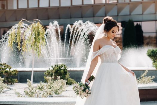 Portrait of the bride in the city near the fountain.A stunning young bride with curly hair . Wedding day. . Beautiful portrait of the bride without the groom