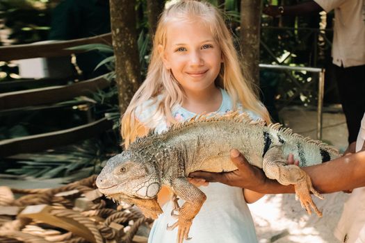 Summer portrait of a happy little girl in a zoo on the island of Mauritius with an iguana.little girl in the zoo with a crocodile in her arms.