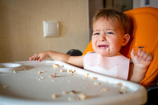 portrait of cute crying baby toddler sitting with dining table