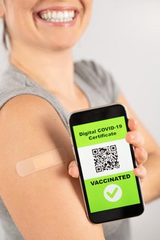 Woman with a plaster on her shoulder after vaccination and demonstrates the QR code on a smartphone