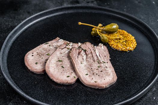 Pork boiled tongue slices on a plate. Black background. Top view.