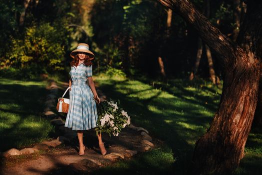 Portrait of a beautiful girl with long hair, a straw hat and a long summer dress with lilac flowers in the garden.