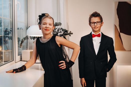 Stylish and elegant boy and girl stand at the window in the interior of the house.