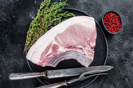 Fresh Raw whole rack of pork loin chops with ribs on a plate with meat fork. Black background. Top view.