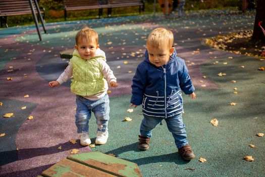 two cute toddlers boy and girl walk in the autumn park together. friendship since childhood concept.