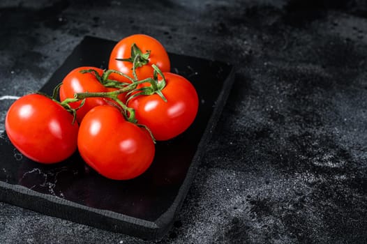 Branch of Red cherry tomatoes on marble board. Black background. Top view. Copy space.
