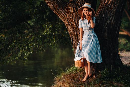 a young beautiful girl in a straw hat and with a straw bag enjoys the view of the lake.