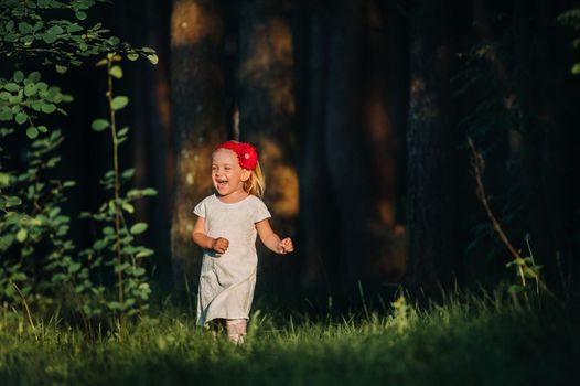 Portrait of a cute little girl runs on a green lawn in a forest. A happy child laughs and smiles. Sunny forest, a ray of sunshine