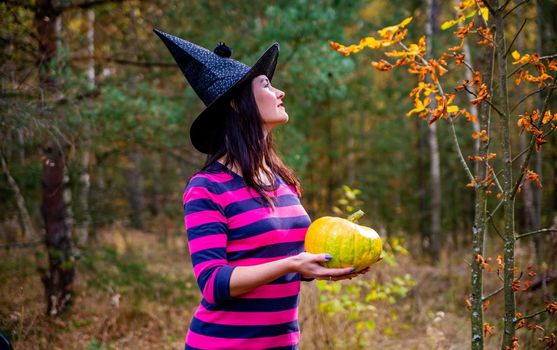 young adult witch with pumpkin in autumn forest