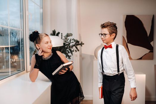 Stylish boy and girl stand near the window with books in their hands.