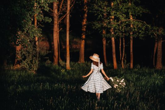 Portrait of a beautiful girl with long hair, a straw hat and a long summer dress with lilac flowers in the garden.