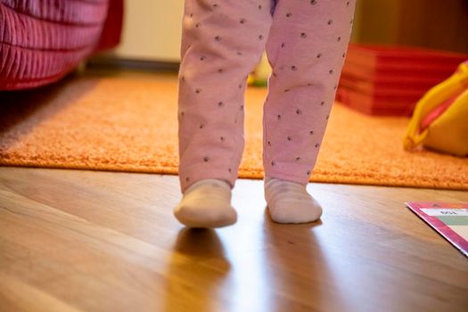 the legs of a small child are walking around the room. baby's first steps concept. no face. happy parenthood