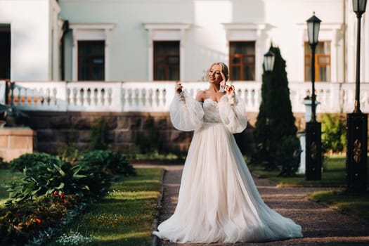 Beautiful bride in a luxurious wedding dress on a green natural background. Portrait of a happy bride in a white dress smiling on the background of the estate