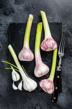 Raw Spring young garlic bulbs and cloves on marble board. Black background. Top view.