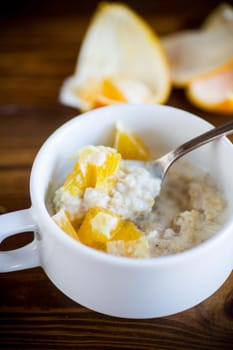 cooked boiled sweet oatmeal with oranges in a bowl on a wooden table