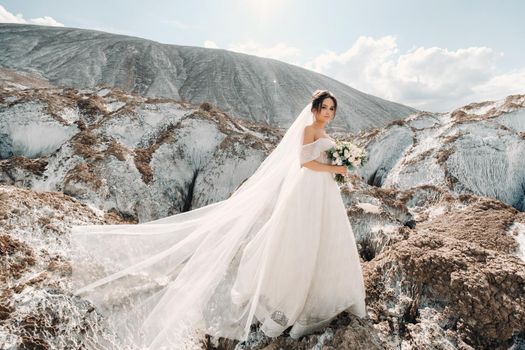 Beautiful bride in a wedding dress with a bouquet on the top of the salt mountains. A stunning young bride with curly hair . Wedding day. . Beautiful portrait of the bride without the groom