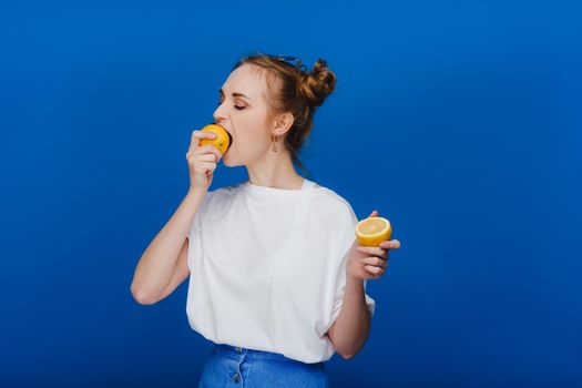 Beautiful brunette woman takes a bite of a lemon. Girl on a blue background.