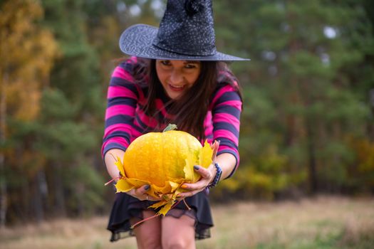 beautiful witch holds out a pumpkin to the camera in the autumn forest