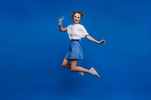happiness, freedom, movement and people concept - smiling young woman jumping in the air over blue background,