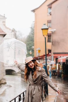 beautiful romantic girl in a coat and hat with a transparent umbrella in Annecy. France. The girl in the hat in France.