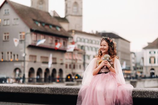 a little girl in a pink Princess dress with a bouquet in her hands walks through the old city of Zurich.Portrait of a girl in a pink dress on a city street in Switzerland.