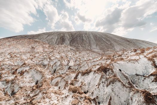 A beautiful couple of lovers posing in a white salt mountain. A young woman in a stylish wedding dress and a beautiful stylish man in a gray suit. The concept of the wedding day