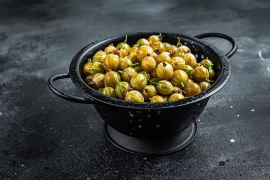 Fresh green gooseberries in a colander. Black background. Top view.