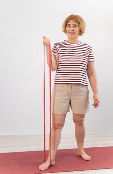 An elderly woman is engaged in fitness with an elastic band on a white background.