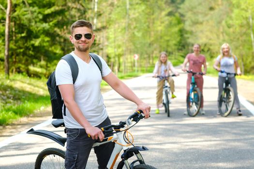 A group of cyclists with backpacks ride bicycles on a forest road enjoying nature.