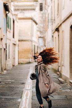 a beautiful romantic girl in a coat with her hair down runs through the old city of Avignon. France. Girl in a coat in France.