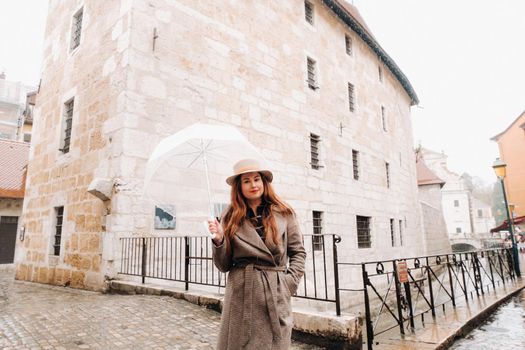 beautiful romantic girl in a coat and hat with a transparent umbrella in Annecy. France. The girl in the hat in France.
