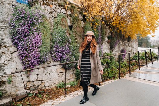 a beautiful romantic girl in a coat and hat walks in Annecy. France. Girl in a hat in France on the background of flowering plants.