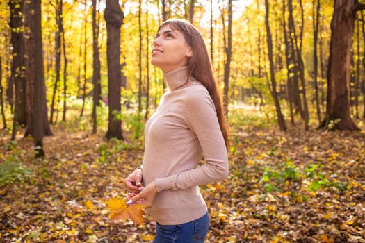 portrait of young beautiful woman in autumn park in sun shines. smiling young woman looking at the sky