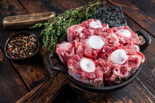 Raw veal beef Oxtail Meat on butcher wooden board with cleaver. Dark wooden background. Top view.