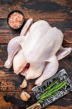 Whole chicken, raw poultry on a butchery table with meat cleaver. Dark Wooden background. Top view.