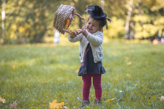 little cute witch playing with a basket of leaves in the autumn park