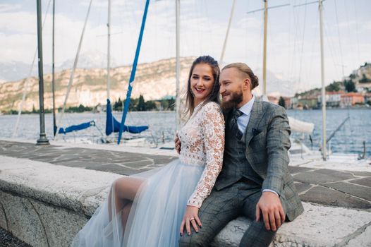 Italy, Lake Garda. A beautiful couple on the shores of lake Garda in Italy at the foot of the Alps.A man and a woman sit on a pier in Italy.