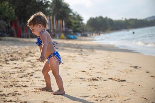 adorable toddler girl playing on sandy beach of tropical island. summer holiday