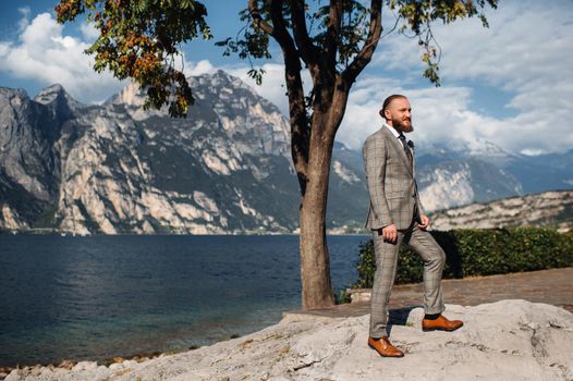 A bearded man in a strict gray three-piece suit with a tie in the background of the Alps near lake Garda,Italy.