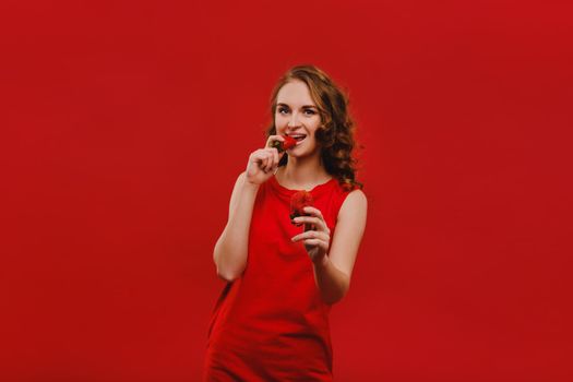 Sweet strawberries. Beautiful bright girl in retro style eating a strawberry. Happy pin up woman isolated on pink wall background eating strawberry