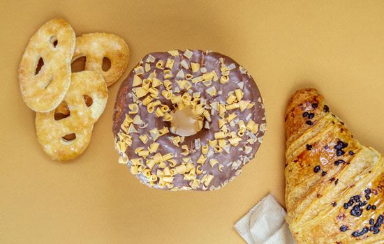 Fresh chocolate donut, croissant and biscuit isolated on delicate coffee or brown background. Delicious desserts. Sweet food concept for your design and print. Top view, flat lay. Copy space