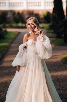 Beautiful bride in a luxurious wedding dress holds a bouquet of white roses and greens on a green natural background. Portrait of happy bride in white dress smiling on wall background with greens