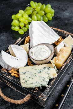 Assorted Cheese platter with Brie, Camembert, Roquefort, parmesan, blue cream cheese, grape and nuts. Black background. Top view.