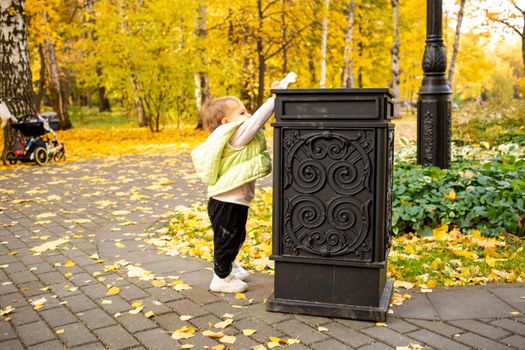 litte toddler throws trash into trash can in autumn park. instilling cultural norms from birth