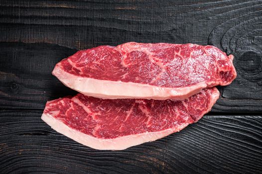 Raw rump steak or top sirloin cap beef meat steaks on butcher table. Black wooden background. Top view.