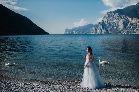 a girl in a smart white dress walks along the embankment of lake Garda.A woman is photographed against the background of a mountain and lake in Italy.Torbole.