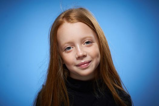 redhead girl with freckles on her face posing close-up blue background. High quality photo