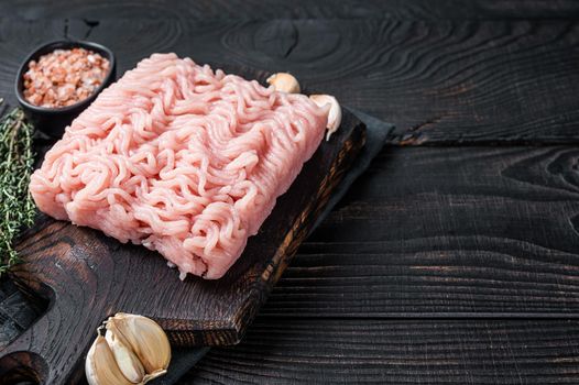 Fresh Raw mince or ground chicken meat on wooden chopping board with thyme. Black wooden background. Top view. Copy space.